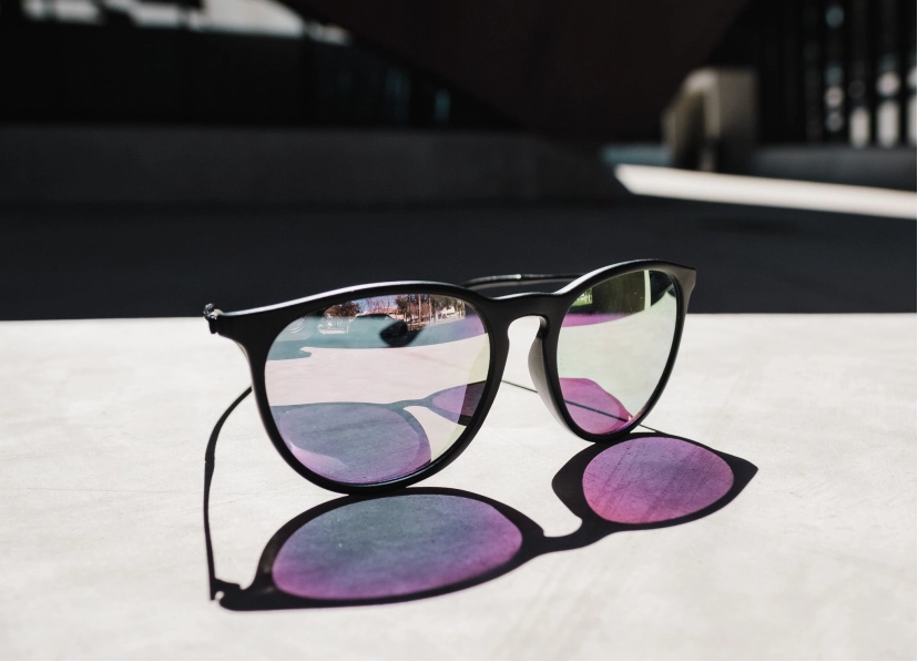 Black round sunglasses with purple-pink gradient lenses resting on a white surface